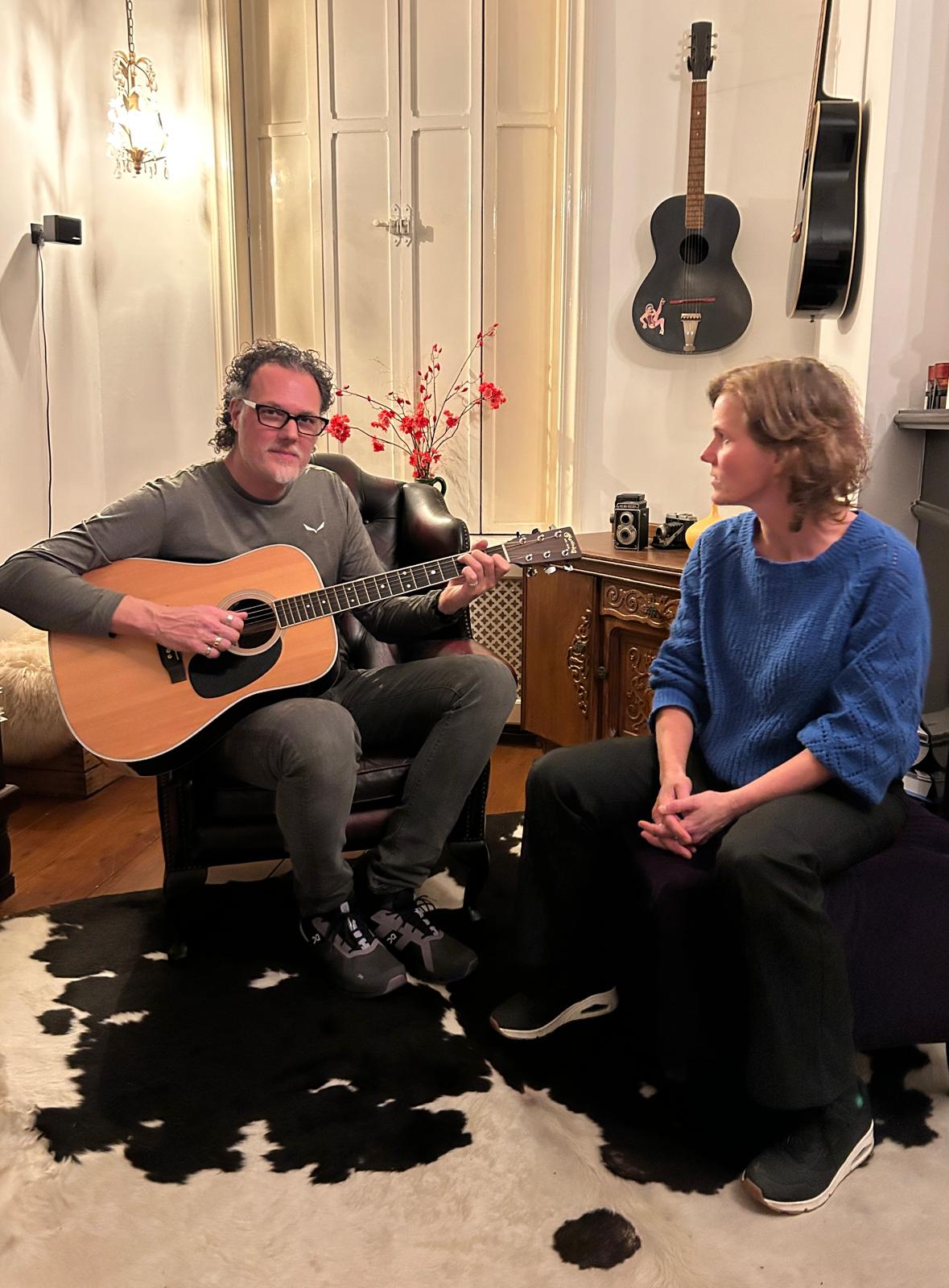 Paul op de gitaar en Cindy zit er zingend naast in een huiskamer setting