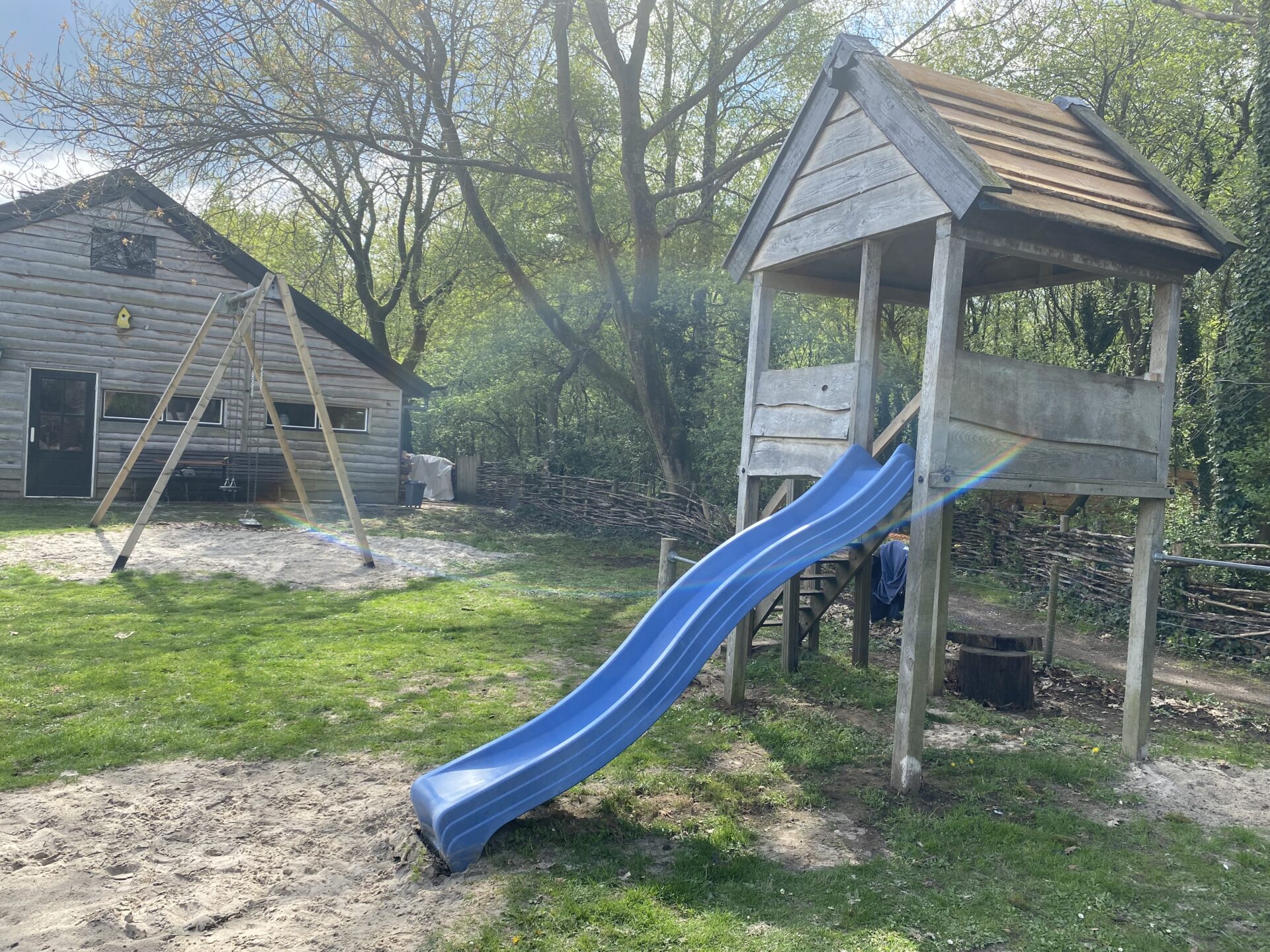 Speeltuin met tuinshuisje met glijbaan en schommel op de achtergrond