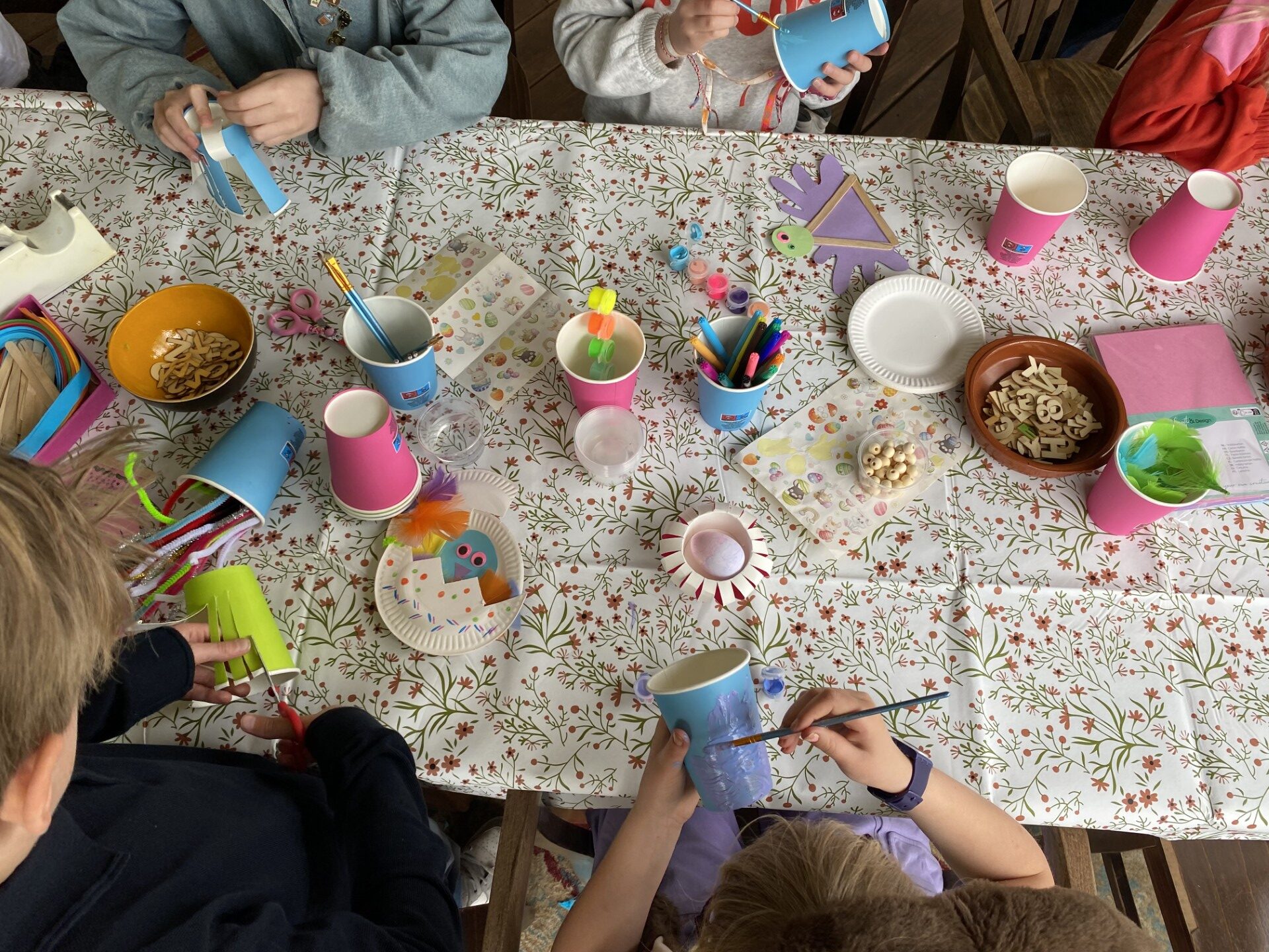 gedekte tafel met allerlei knutselspullen en kinderhandjes die mooie dingen aan het maken zijn