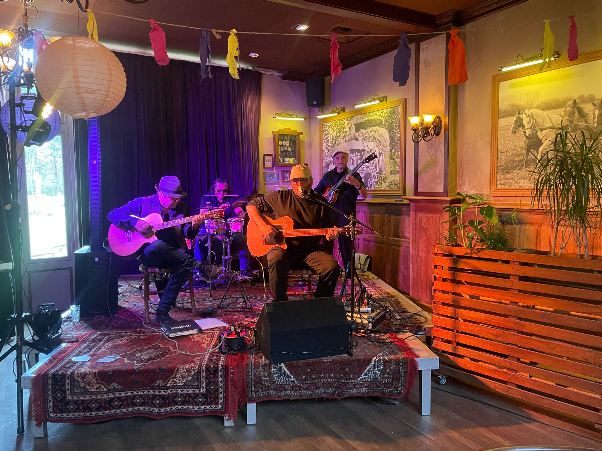 4 mannen op een podium 3 gitaren en een drumstel