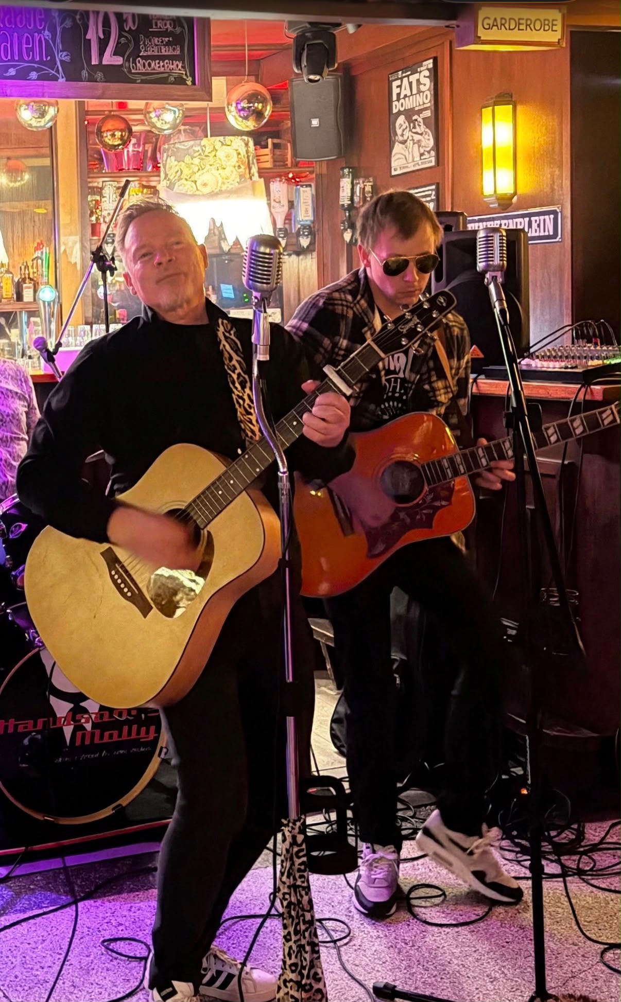 2 heren met een gitaar en zang op een gezellig podium