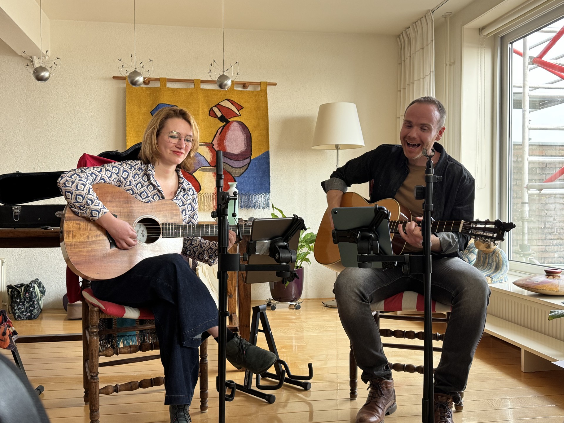 man en een vrouw met gitaar die tegelijkertijd ook zingen in een woonkamer