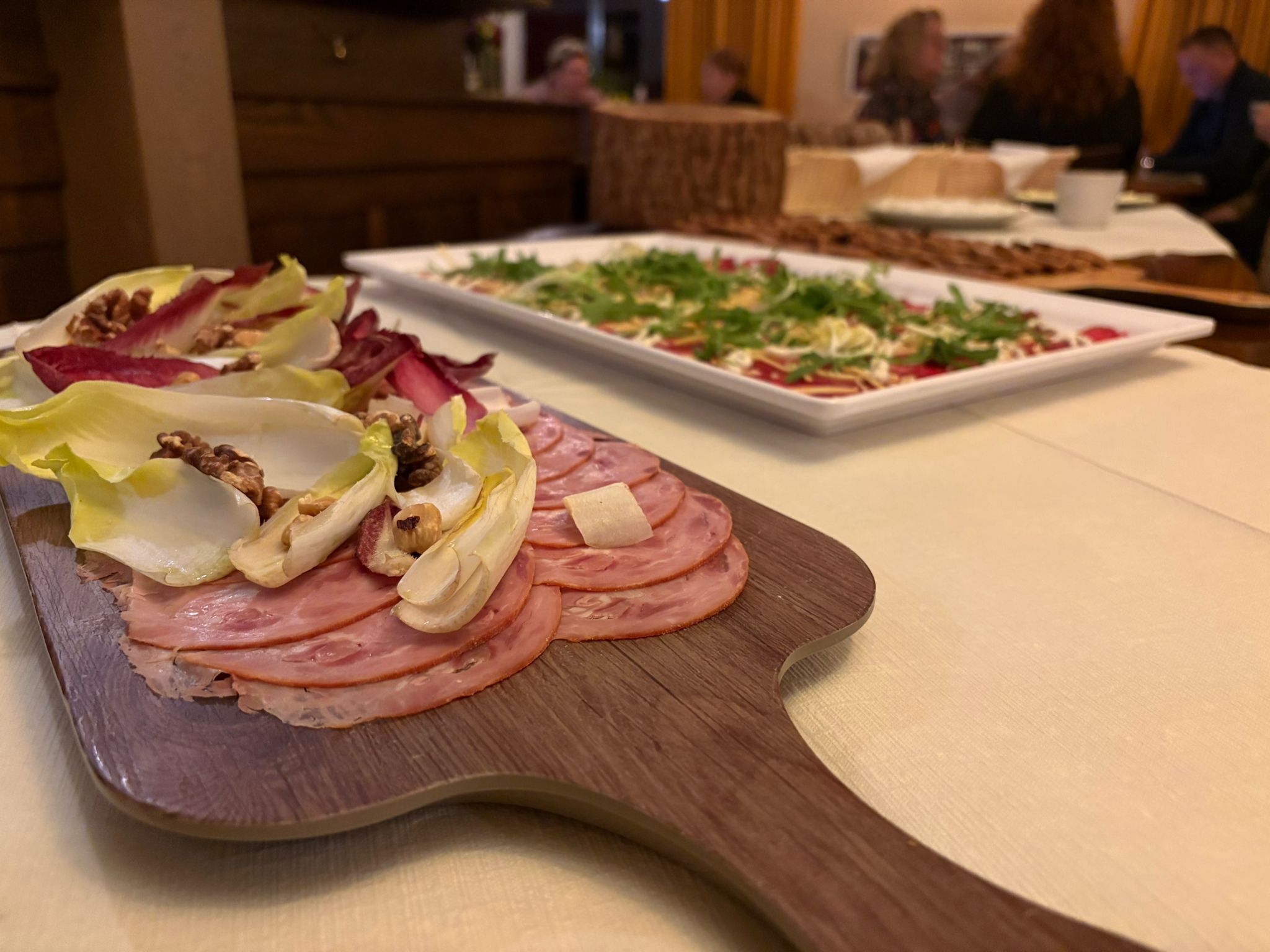 Plank met verschillende hammen en daarachter een schaal met hertencarpaccio